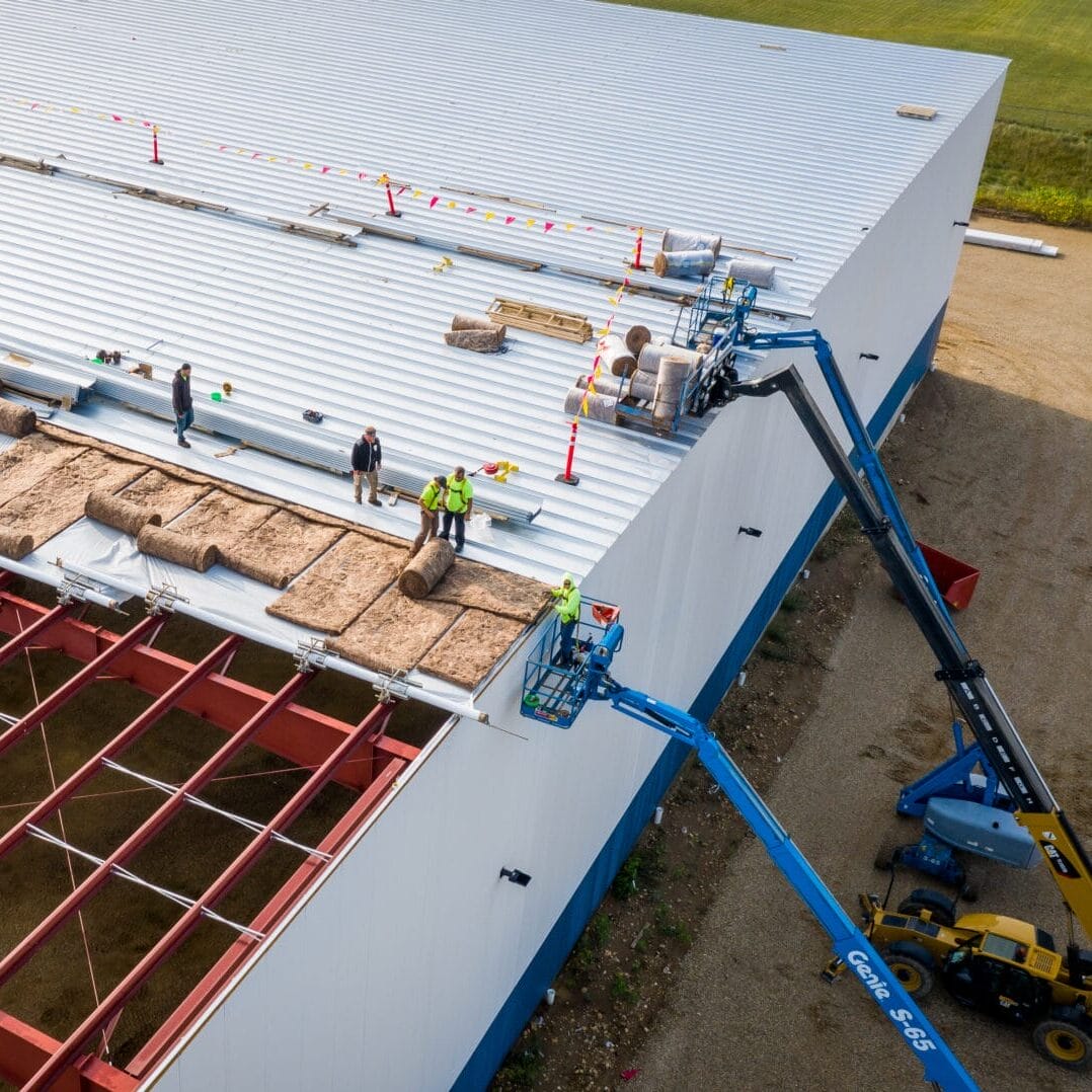 Construction Workers Installing Roof Panels On A Warehouse.